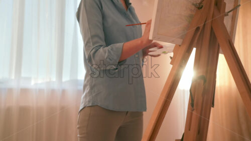 Video - Caucasian woman painting a picture with a palette in her hands, indoors. Slow motion
