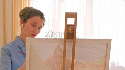 Video - Caucasian woman painting a picture with a palette in her hands and listening music with earphones indoors