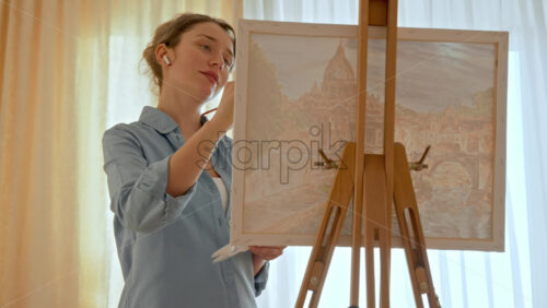 Video - Caucasian woman painting a picture with a palette in her hands and listening music with earphones indoors