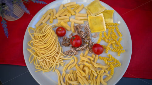 Video - White plate with a variety of uncooked pasta, noodles and cherry tomatoes on it