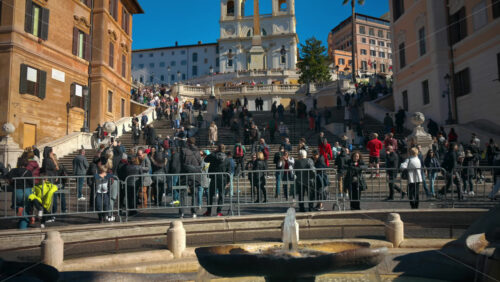 Video - Rome, Italy - February 14, 2024: Tourists walking on Spanish Steps near the baroque-style Fountain of the Boat in sunlight. Church of Santissima Trinità dei Monti in background