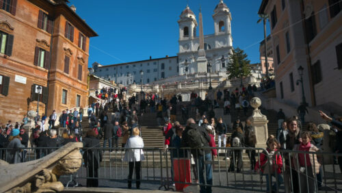 Video - Rome, Italy - February 14, 2024: Tourists walking on Spanish square near the baroque-style Fountain of the Boat in sunlight. Church of Santissima Trinità dei Monti in background
