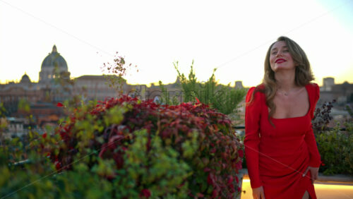 Video - Beautiful young woman in red dress dancing near greenery with the Saint Peter's Basilica in background. Rome, Italy