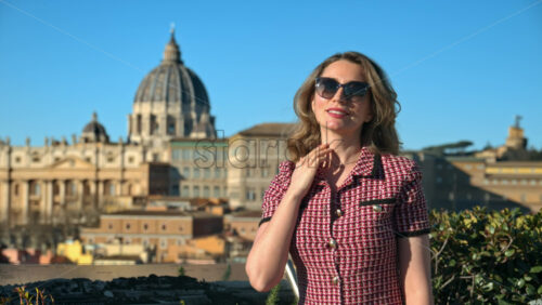 Video - Blonde young woman in sunglasses smiles with Vatican city in background. Saint Peter's Basilica at sunset. Rome, Italy