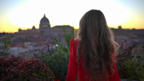 Video - Young woman in red dress dancing near greenery with the Saint Peter's Basilica in background. Rome, Italy