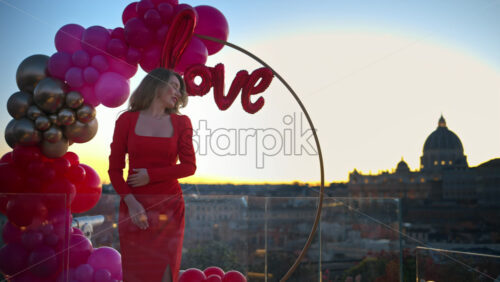 Video - Beautiful young woman in red dress dancing at sunset near the red and pink balloon arch spelling out the word "love". Vatican city in background. Rome, Italy