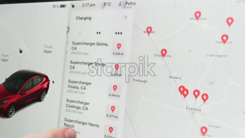 Video - Chisinau, Moldova - January 23, 2024: Male hands scrolling the charging locations list on the touch screen of the red Tesla Model 3 electric car. Light theme