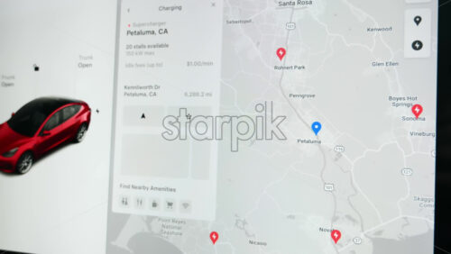 Video - Chisinau, Moldova - January 23, 2024: Male hands choosing the pins on the map, representing the closest charging location in the area. Touch screen of the red Tesla Model 3 electric car. Light theme