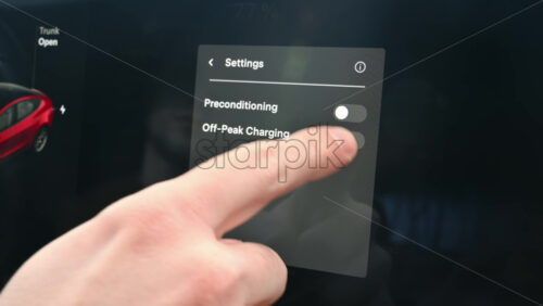 Video - Chisinau, Moldova - January 23, 2024: Male hands turn on the preconditioning and off-peak charging settings on red Tesla Model 3 electric car touch screen and read the informations. Dark theme