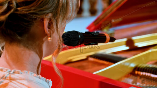 Video - Woman singing into the microphone and playing a red piano