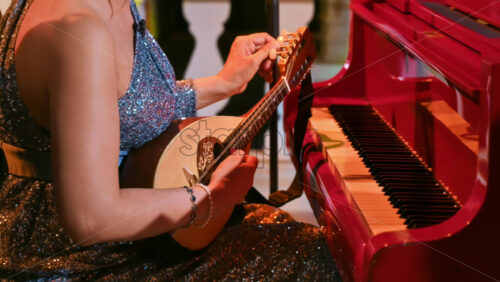 Video - Dressed-up woman playing the mandolin near a red piano