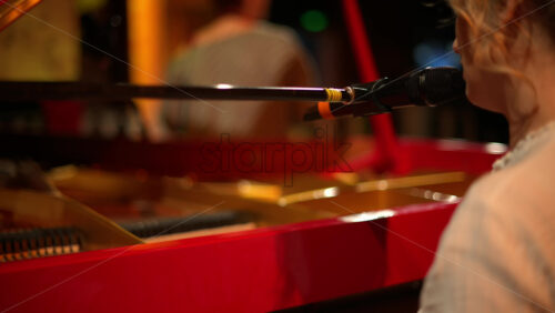 Video - Woman singing into the microphone and playing a red piano