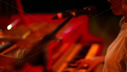 Video - Woman singing into the microphone and playing a red piano