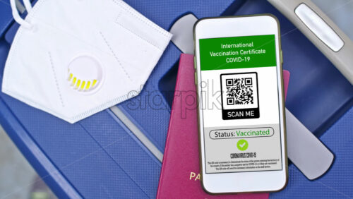 Video - Passport and smartphone with International Vaccination Certificate COVID-19 QR code on suitcase with mask