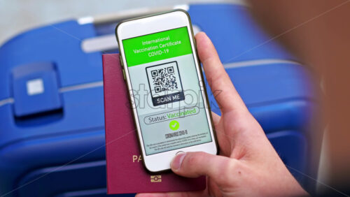 Video - Male hand holding passport and smartphone with International Vaccination Certificate COVID-19 QR code, suitcase
