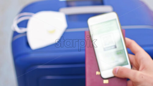 Video - Male hand holding passport and smartphone with International Vaccination Certificate COVID-19 QR code, suitcase with mask