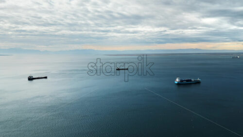 Video - Aerial drone view of cargo ships floating in the middle of a large body of water. Clear sky, calm blue water