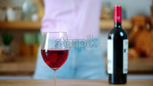 Video - A glass and a bottle of red wine standing on the table in front of a woman dancing in the kitchen