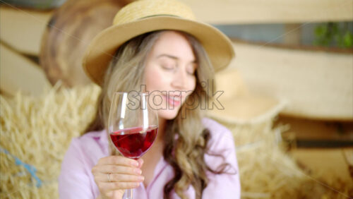 Video - Woman enjoying a glass of red wine in the barn near square hay bales, in daylight