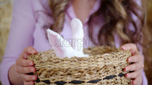Video - Woman playing with a white bunny in the barn near square hay bales, in daylight