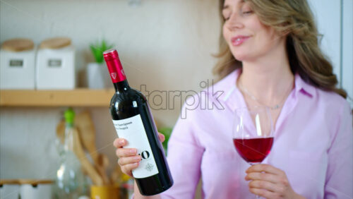 Video - Woman holding a glass and a bottle of red wine in the kitchen