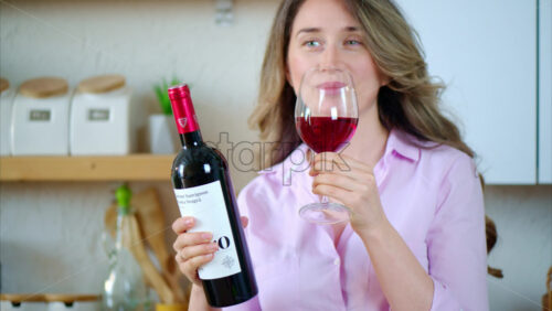 Video - Woman holding a bottle and drinking a glass of red wine in the kitchen