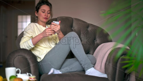 Video - Caucasian woman sitting on a chair is on her smartphone. Table with tea and fruits nearby