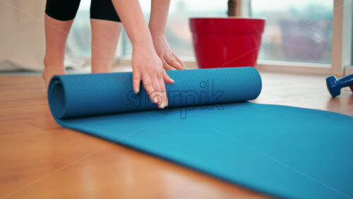 Video - Close up of a girl rolling out blue yoga matt indoor. Preparing to meditate
