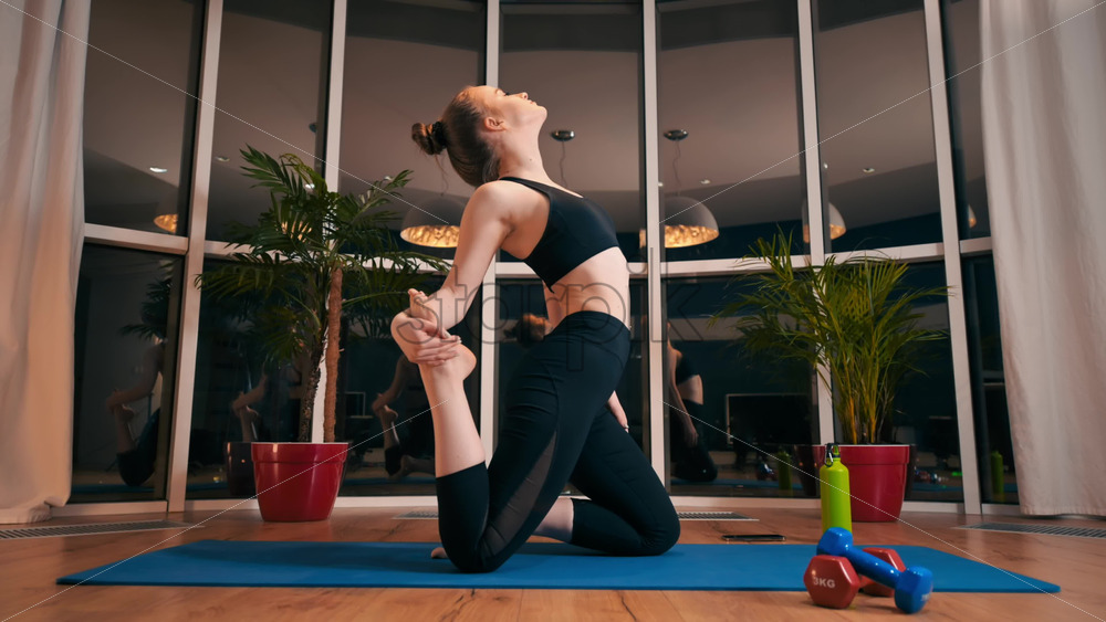 Video - Young woman stretching while doing yoga. Indoor training in apartment, quarantine. Night