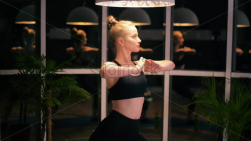 Video - Young woman stretching hands while doing yoga. Indoor training in apartment, quarantine. City lights on background. Night