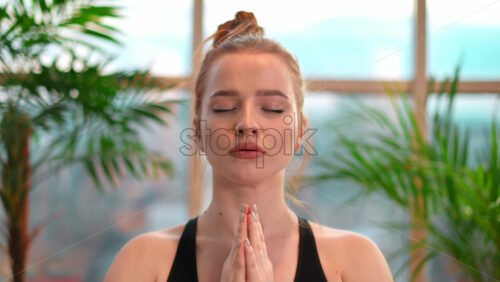 Video - Young woman in yoga prayer pose meditating indoors in apartment. City on background.