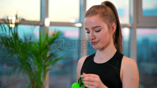 Video - Young woman drinking water after workout with city on background. Indoor training in apartment, quarantine