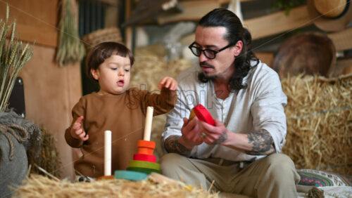 Video - Father playing with his son with colourful, ecological wooden toys in a barn, near square hay bales