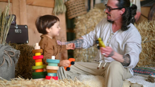 Video - Father playing with his son with colourful, ecological wooden toys in a barn, near square hay bales