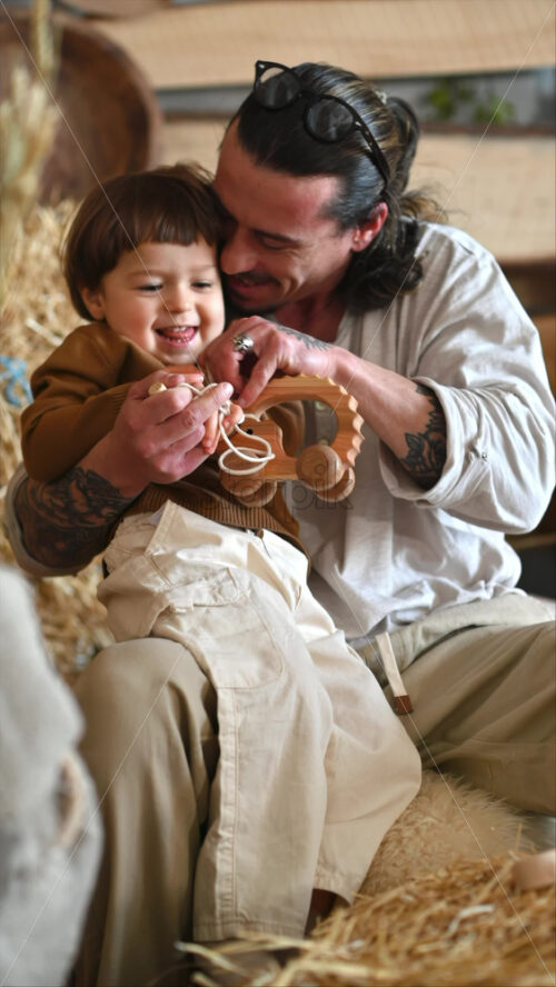 Video - Father playing with his son with ecological wooden toy in a barn, near square hay bales