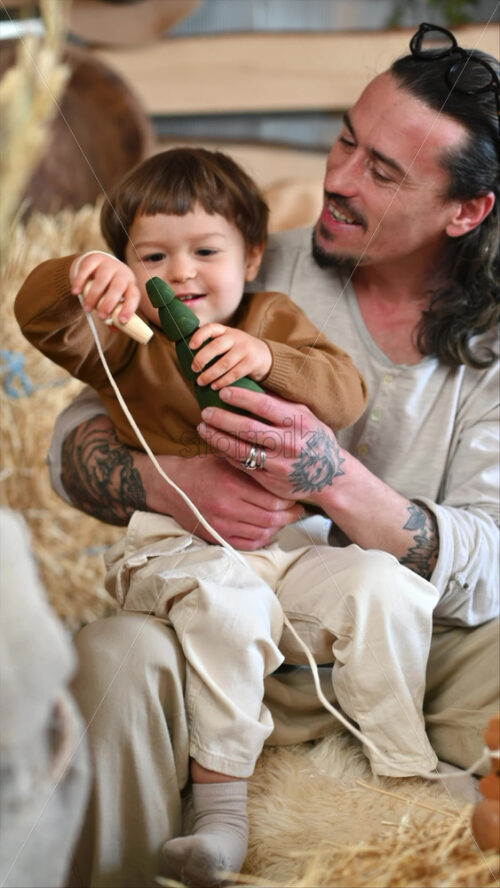 Video - Father playing with his son with ecological wooden toys in a barn, near square hay bales