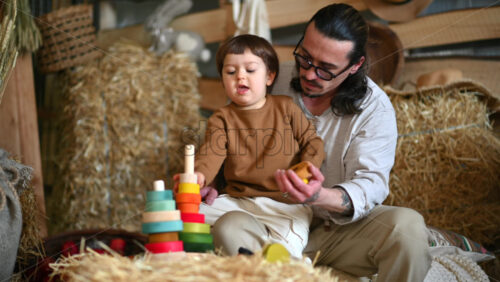 Video - Father playing with his son with colourful, ecological wooden toys in a barn, near square hay bales