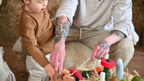 Video - Father playing with his son with colourful, ecological wooden toys in a barn, near square hay bales