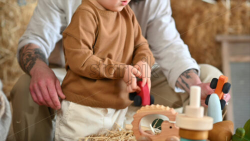 Video - Father playing with his son with colourful, ecological wooden toys in a barn, near square hay bales