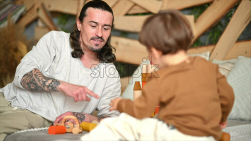 Video - Father playing with his son with colourful, ecological wooden toys on the bed