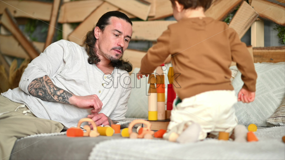 Video - Father playing with his son with colourful, ecological wooden toys on the bed