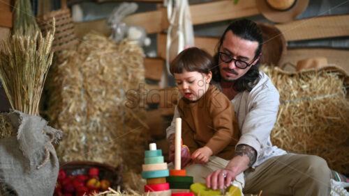 Video - Father playing with his son with colourful, ecological wooden toys in a barn, near square hay bales