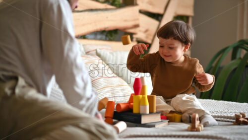 Video - Father playing with his son with colourful, ecological wooden toys on the bed