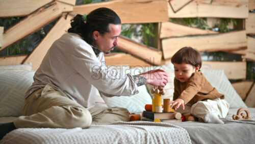 Video - Father playing with his son with colourful, ecological wooden toys on the bed