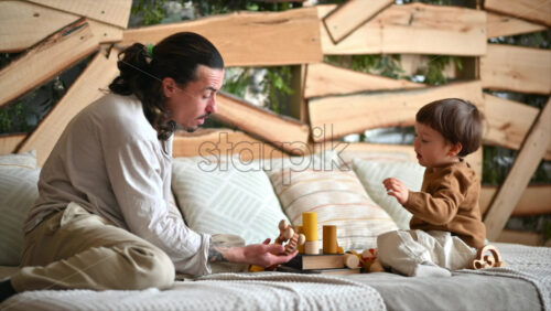 Video - Father playing with his son with colourful, ecological wooden toys on the bed