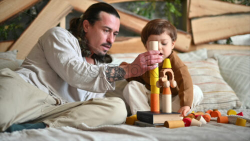 Video - Father playing with his son with colourful, ecological wooden toys on the bed