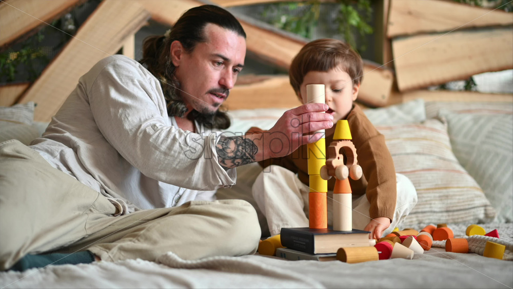 Video - Father playing with his son with colourful, ecological wooden toys on the bed