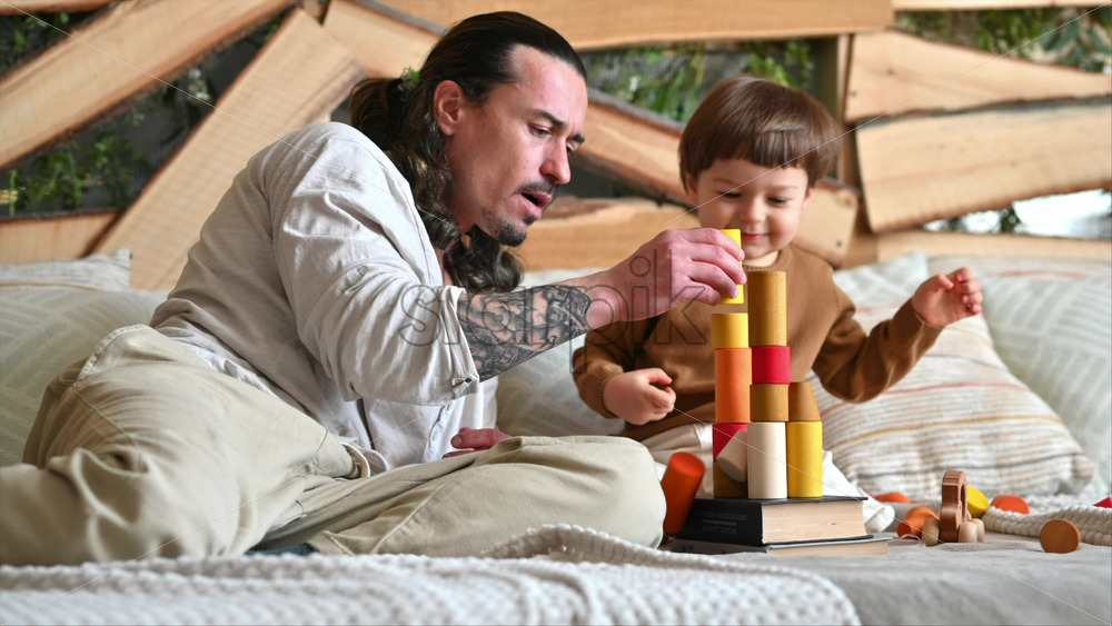 Video - Father playing with his son with colourful, ecological wooden toys on the bed