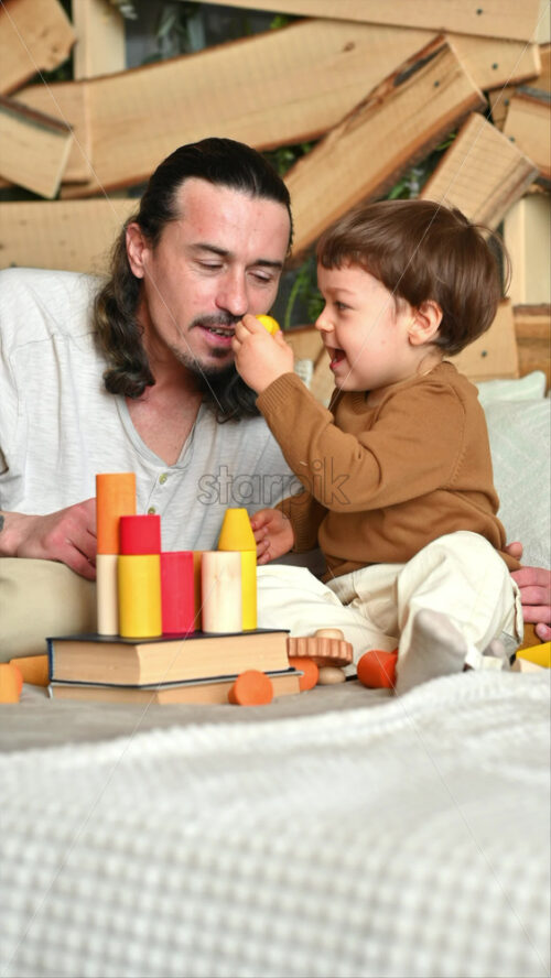 Video - Father playing with his son with colourful, ecological wooden toys on the bed
