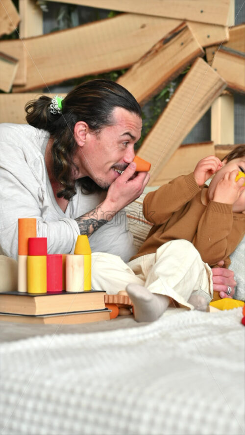 Video - Father playing with his son with colourful, ecological wooden toys on the bed